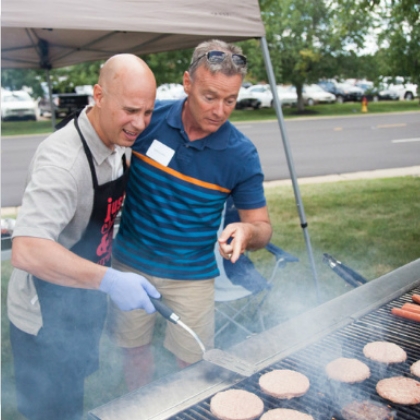 Two men grilling burgers at an outdoor event