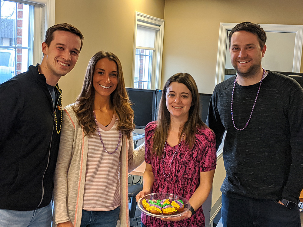 Four people standing together, smiling, and holding a plate of colorful cookies