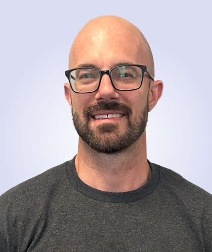 Portrait of a man with a bald head, glasses, and a beard, wearing a gray shirt.