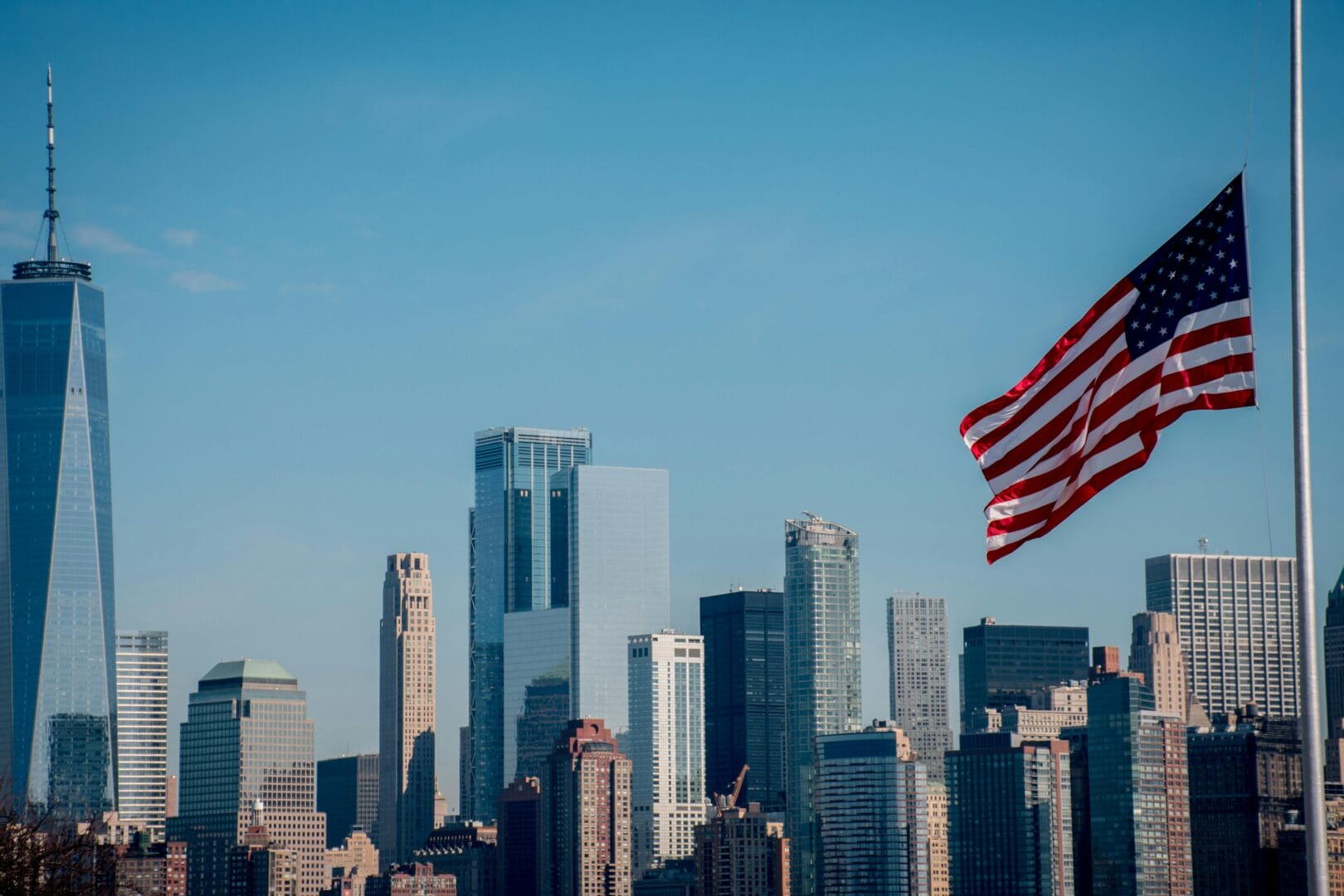 American flag waving in the foreground with a city skyline in the background.