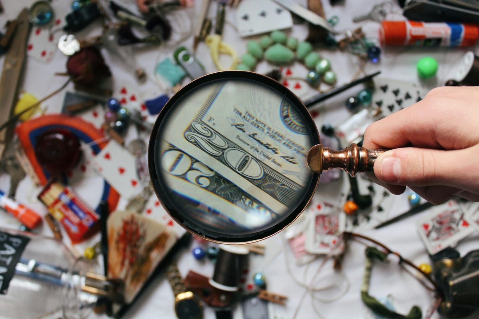 Magnifying glass focusing on a $20 bill among various scattered items.