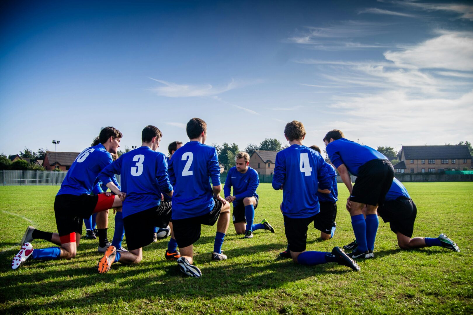 Soccer team huddled together on a field, wearing blue jerseys with numbers on their backs.