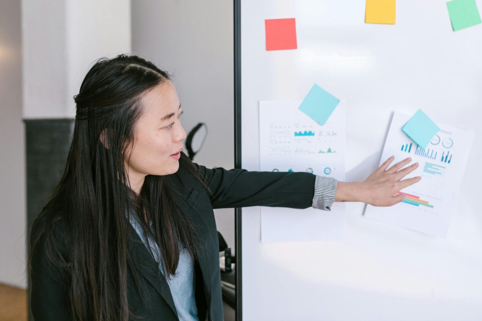Woman pointing at a chart with various data points, including a bar graph and a pie chart, while another person watches.