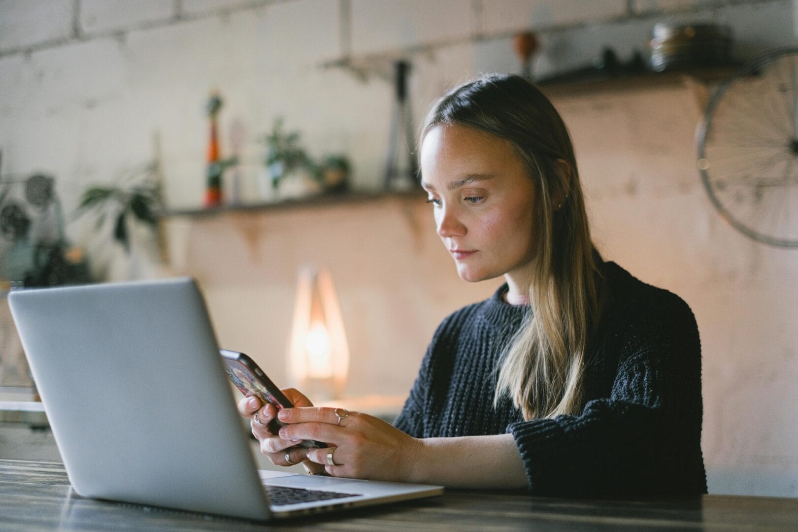 Woman working on a laptop while holding a smartphone.