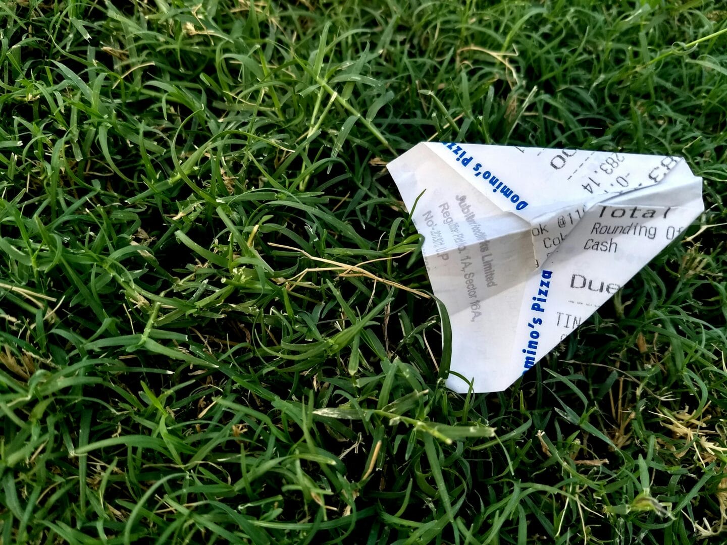 Paper airplane made from a receipt lying on grass.