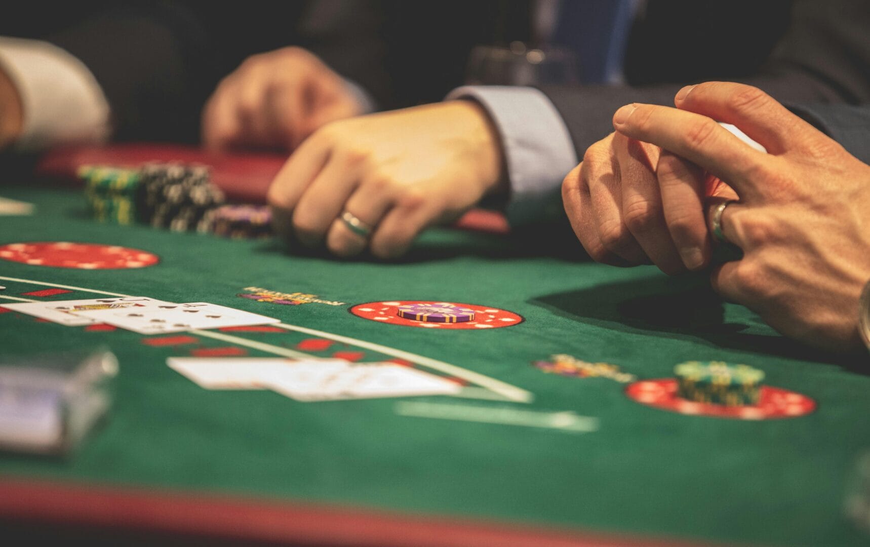 Hand holding poker chips on a casino table with cards and chips scattered around.